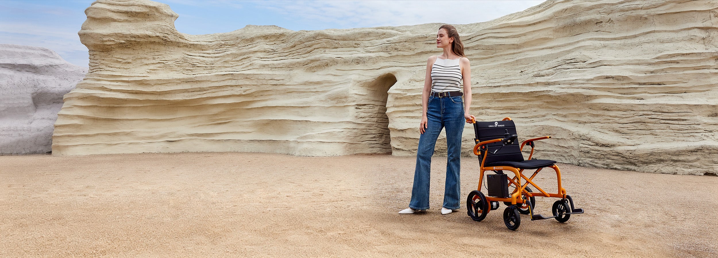 A woman stands outdoors in a desert next to an OAS Air Carbon electric folding wheelchair.